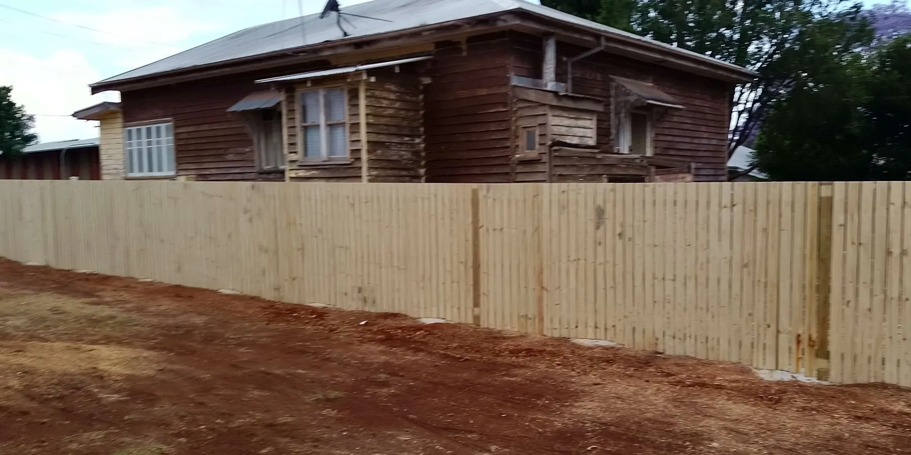 A new timber paling boundary fence on freshly turned red soil
